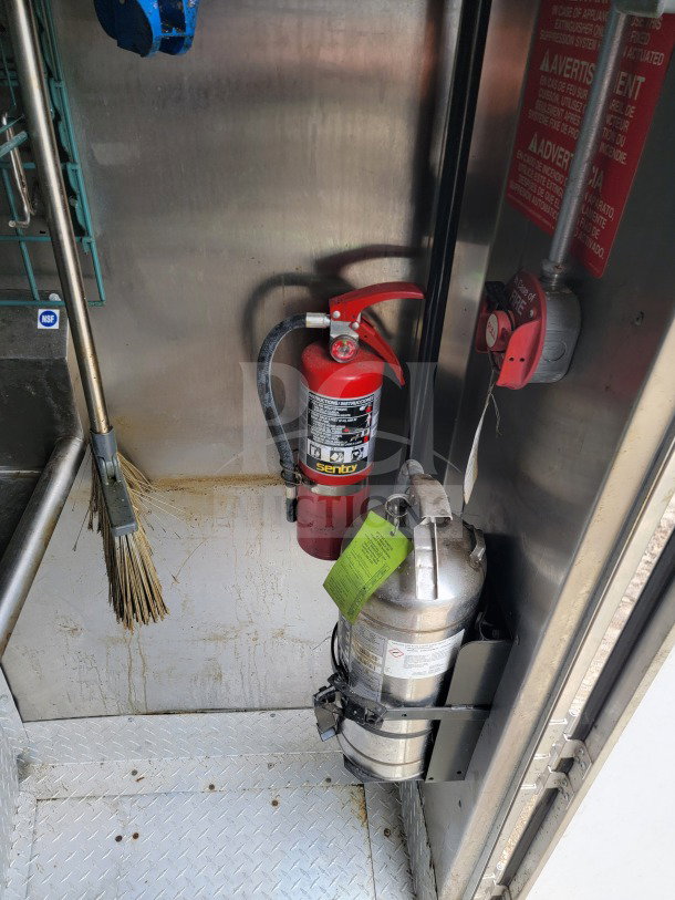 Fire extinguishers and safety labels inside BT&S 2021 mobile kitchen trailer, showcasing interior features.