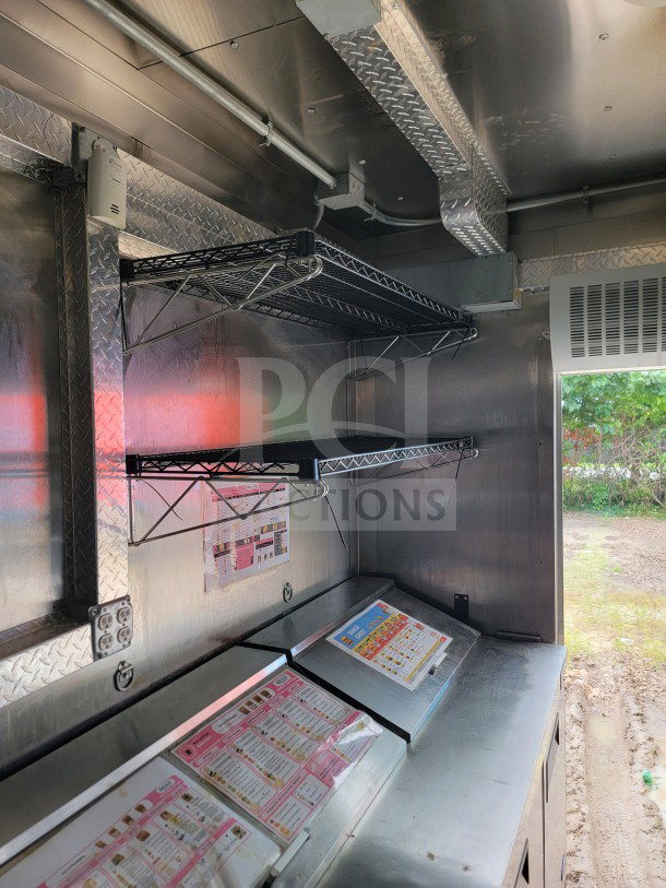 Interior of 2021 BT&S 8.5' x 24' mobile kitchen trailer with stainless steel surfaces, wire shelving, and menu displays.