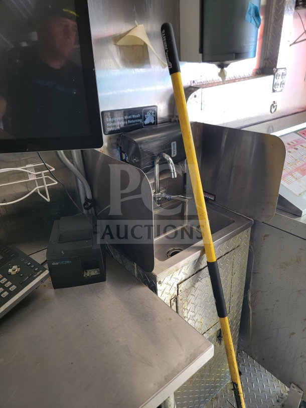 Inside view of 2021 BT&S mobile kitchen trailer, featuring a stainless steel sink, handwashing sign, and cleaning tool.