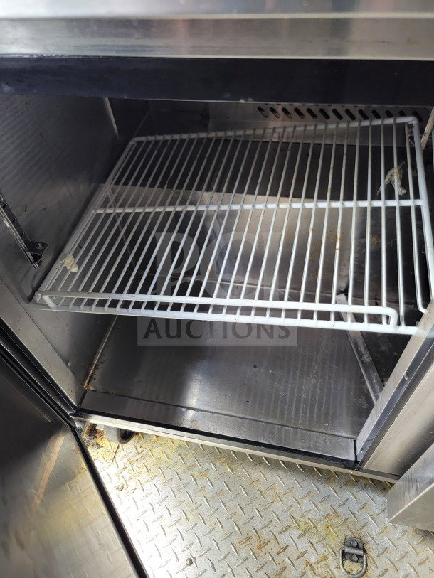Opened stainless steel cabinet with wire shelving inside a 2021 BT&S mobile kitchen trailer. Clean interior, sturdy design.
