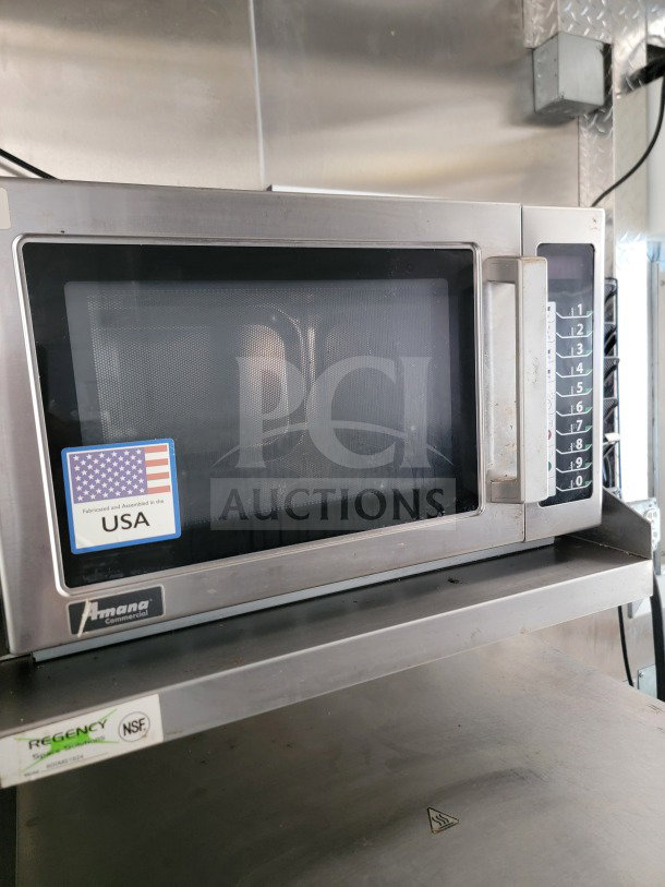 Amana commercial microwave in mobile kitchen trailer. Features USA fabrication label. Positioned over stainless steel surface.