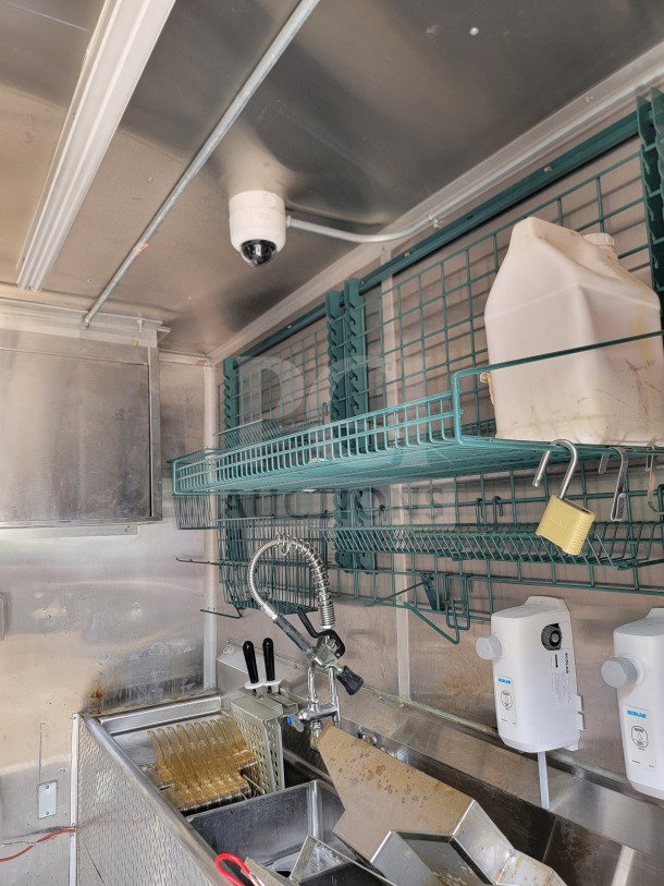 Inside view of a 2021 Titanium Cargo 8.5' x 24' mobile kitchen trailer with stainless steel fixtures, fryer, shelving, and security camera.