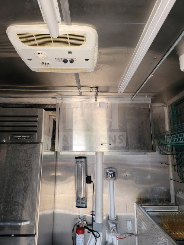 Interior view of a 2021 Titanium Cargo 8.5' x 24' mobile kitchen trailer. Features visible include a ceiling vent, stainless steel surfaces, lighting fixtures, and mounted heating unit.