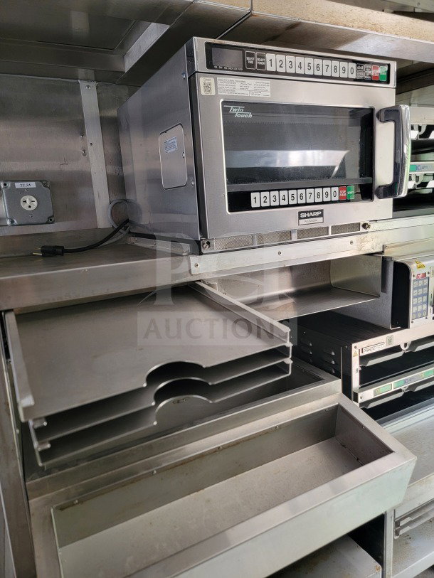Interior of a 2021 Titanium Cargo 8.5' x 24' mobile kitchen trailer, featuring stacked metal trays and a Sharp TwinTouch microwave.