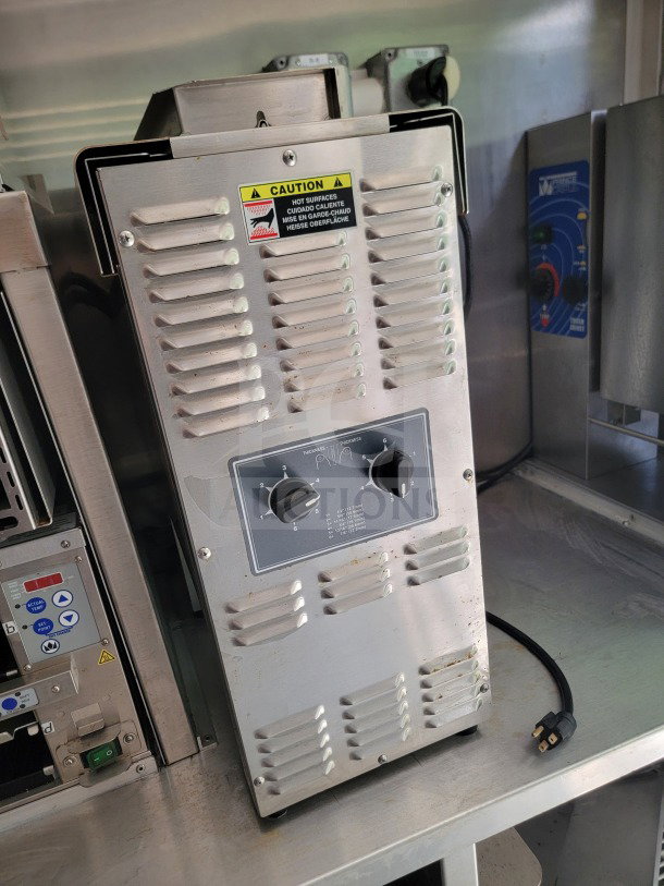 Stainless steel kitchen equipment in a mobile kitchen trailer, featuring control knobs and caution labels.