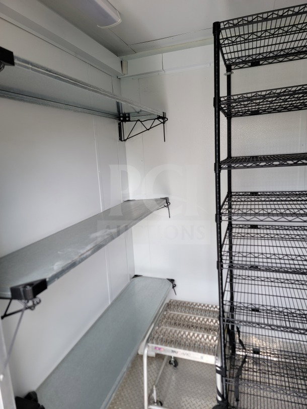 Inside view of a 2021 SDG mobile kitchen trailer with metal shelving and wire racks. Clean and well-organized.