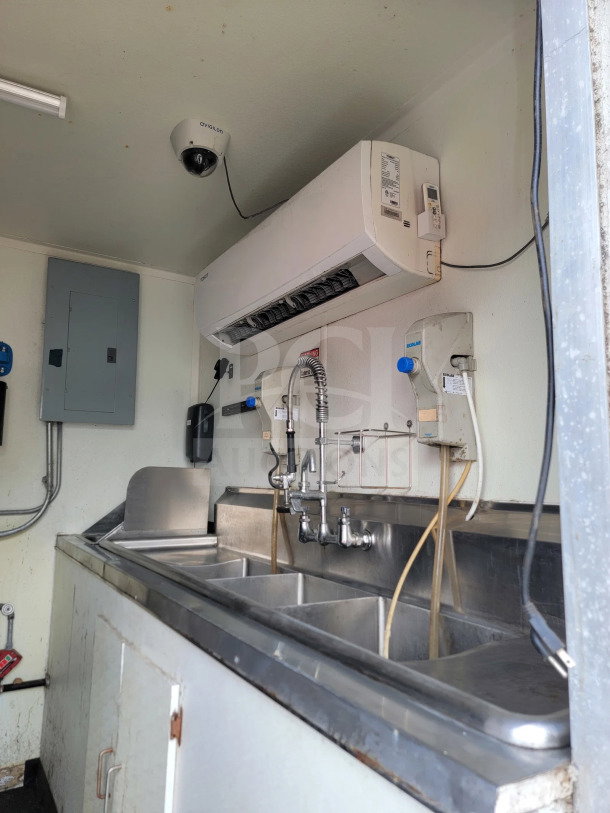 2019 Diamond Cargo mobile kitchen interior with triple sink, stainless steel surfaces, and Avigilon camera installed.