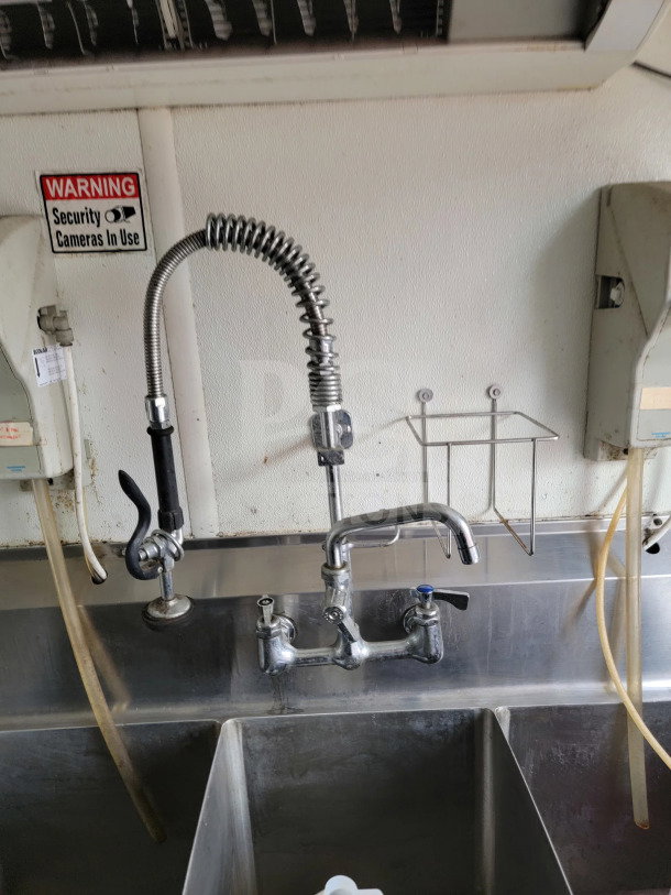 Stainless steel sink with commercial faucet in a 2019 Diamond Cargo mobile kitchen trailer. Security notice on wall.