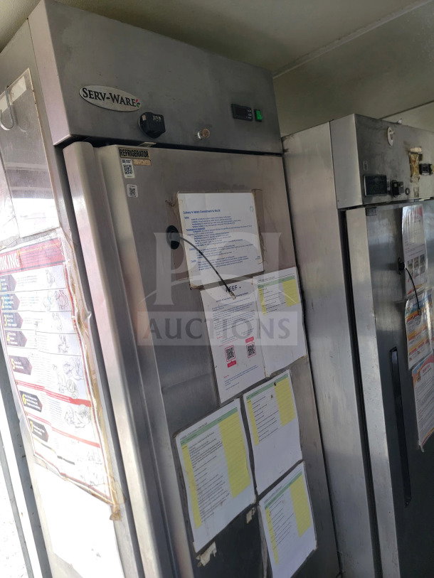 Silver Serv-Ware commercial refrigerator in a mobile kitchen trailer, with instructional documents and labels attached.