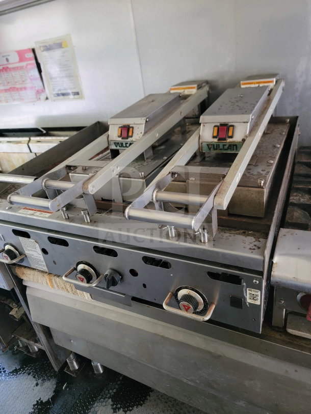 Vulcan gas griddle in mobile kitchen trailer; three control knobs, showing wear; Serv-Ware lineup signage visible.
