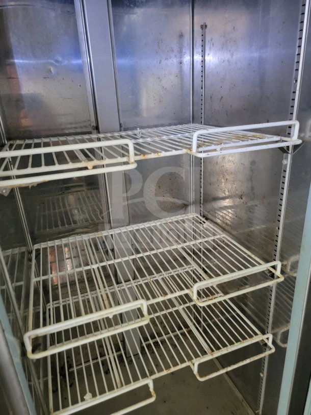 Interior of a commercial refrigeration unit with metal shelving, showing signs of wear and use.