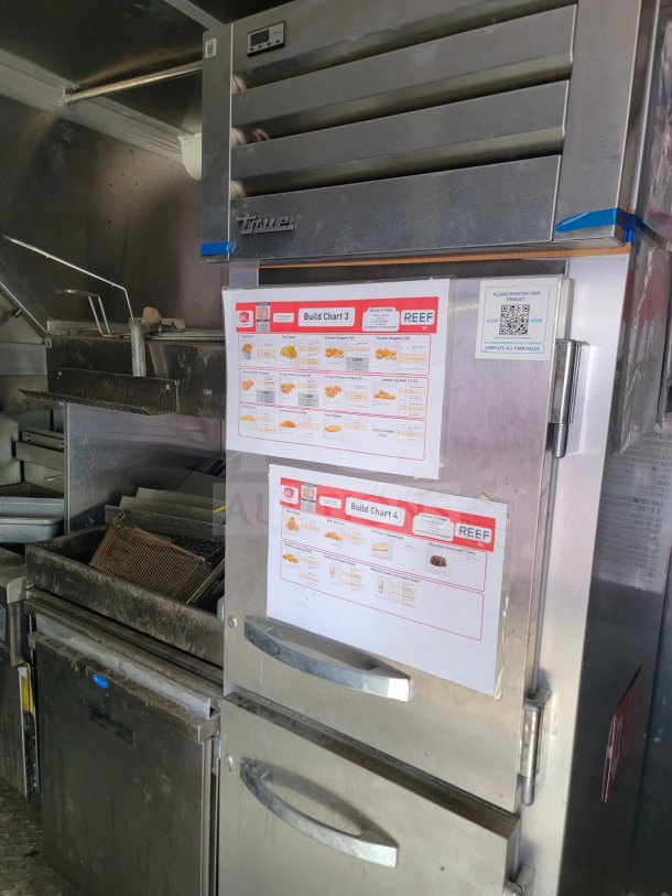 Mobile kitchen trailer interior with True refrigeration unit, order charts, and equipment. Clean, well-maintained condition.