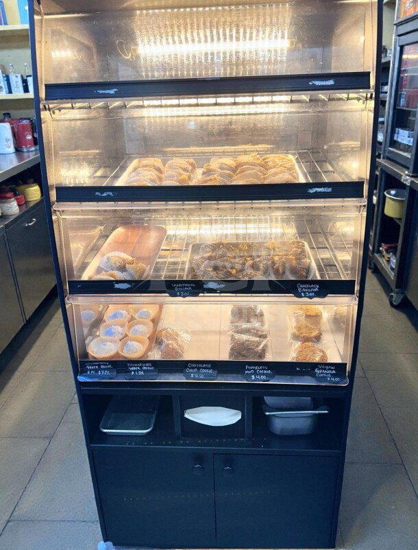 Black non-refrigerated dry display case with three illuminated levels for pastries. Immaculate, fully inspected, operational.