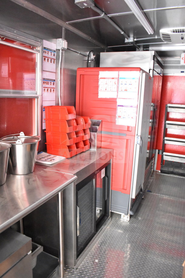 2022 Rock Solid Cargo 8.5x28 food trailer interior with stainless steel counters, red storage bins, and commercial refrigerator.