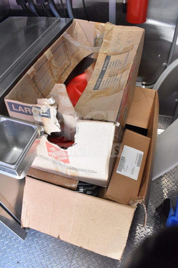 Cardboard boxes inside 2022 Rock Solid Cargo 8.5x28 food trailer. One box is open, showing red contents. Boxes have visible labels and writing.