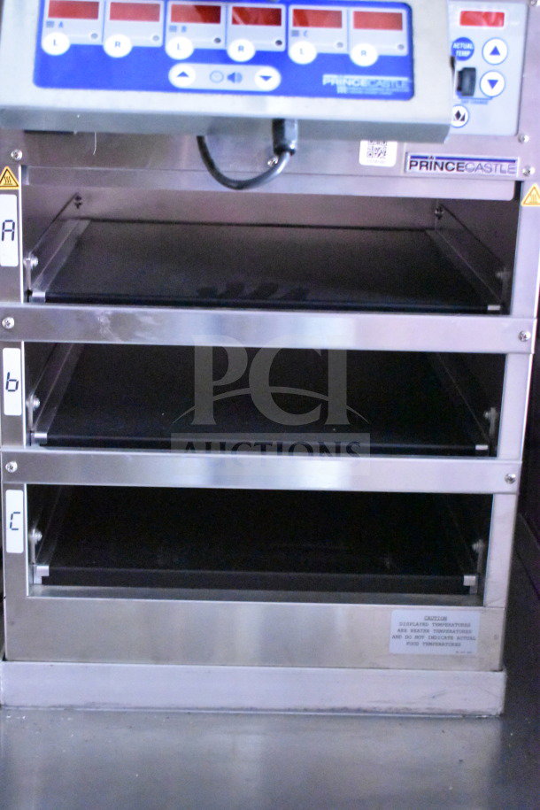 Stainless steel Prince Castle heating unit with multiple shelves, digital controls, and caution label about temperature.