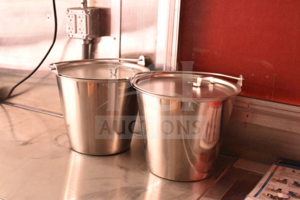 Two stainless steel buckets with lids on a metal countertop inside a 2022 Rock Solid Cargo food trailer.