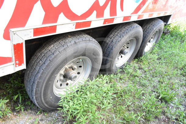 Alt text: 2022 Rock Solid Cargo 8.5x28 Wendy's Food Trailer, triple axle, side view of tires and partial decal, VIN 7H2BE2831ND043576.