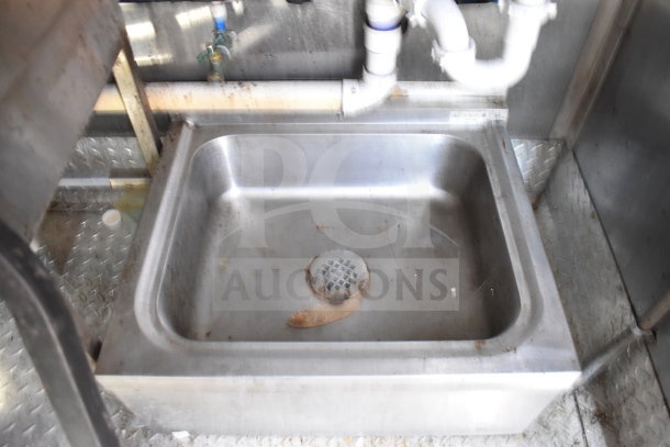 Stainless steel sink inside a Titanium Cargo Trailer food trailer. Includes pipes and metal flooring. Visible wear.
