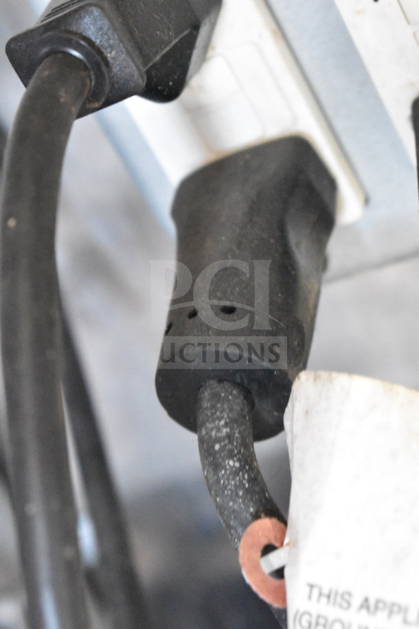 Power cord plugged into a wall outlet with a visible tag indicating electrical grounding requirements.