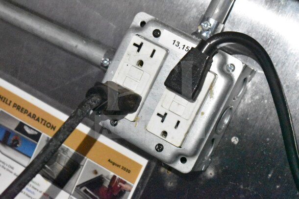 Dual outlet with electrical cords in food trailer, near preparation instructions.