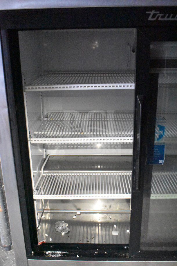 Empty fridge interior in food trailer, featuring multiple wire shelves and a glass door. Visible brand: "True."