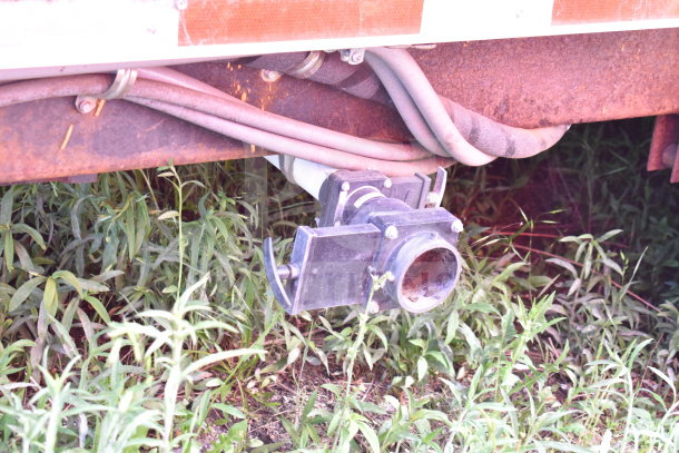 Rusty underside view of 2021 Titanium Cargo Trailer, drainage pipe visible among overgrown grass, VIN 7PLBC2831NM000936.