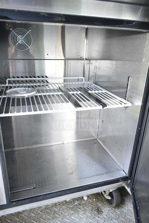 Interior of a Diamond Cargo food trailer, showcasing a stainless steel refrigeration unit. Features shelving and a fan for cooling.