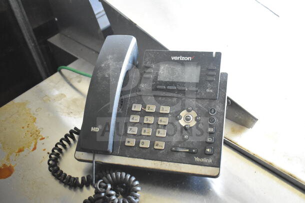 Yealink T41S desk phone on a metal surface, displaying dust and wear, with visible buttons and a Verizon label.