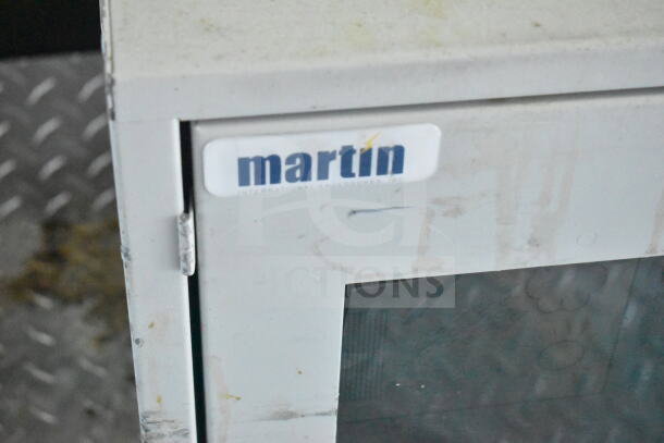 Close-up of a Martin International Enclosures sticker on a metal appliance, part of a 2021 Diamond Cargo food trailer.