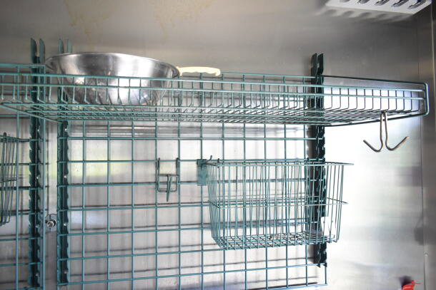 Wire shelving with nested baskets and a hanging hook inside the 2021 Diamond Cargo food trailer. Stainless steel finishes.