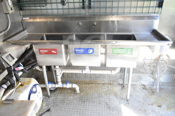 2021 Diamond Cargo food trailer kitchen interior with three-compartment sink labeled wash, rinse, sanitize; stainless steel.