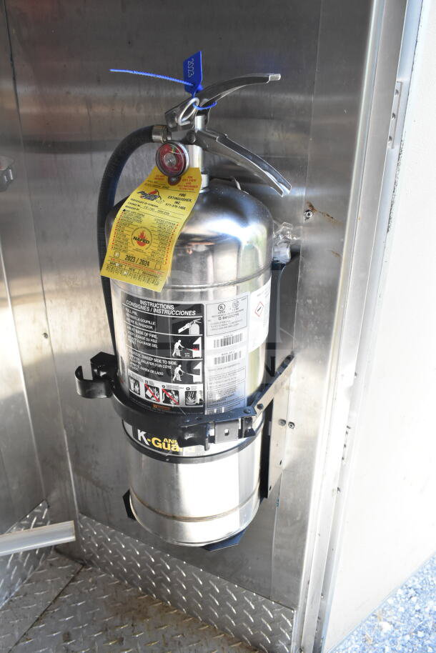 Stainless steel fire extinguisher mounted inside a Diamond Cargo food trailer. Includes inspection tag and safety instructions.