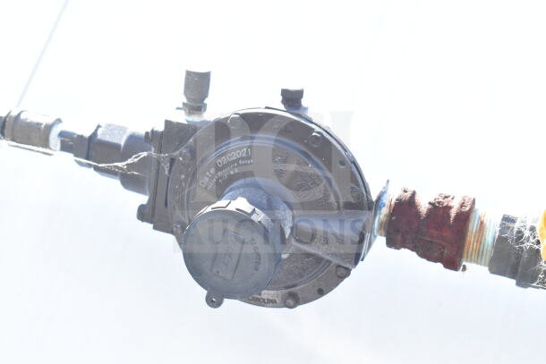Close-up of a pressure regulator with manufacturer markings and a date stamp of 02C2021, connected via pipes.