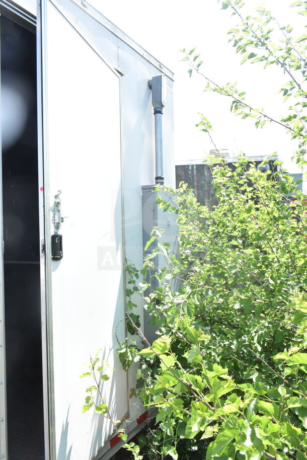 2021 Diamond Cargo 8.5'x24' food trailer, exterior view with open door, partially obscured by foliage; VIN: 53NBE2429M1089847.