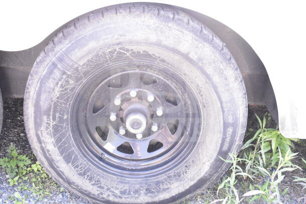 Close-up of a Diamond Cargo food trailer tire, showing visible wear on the tread and wheel rim, set against gravel and grass.