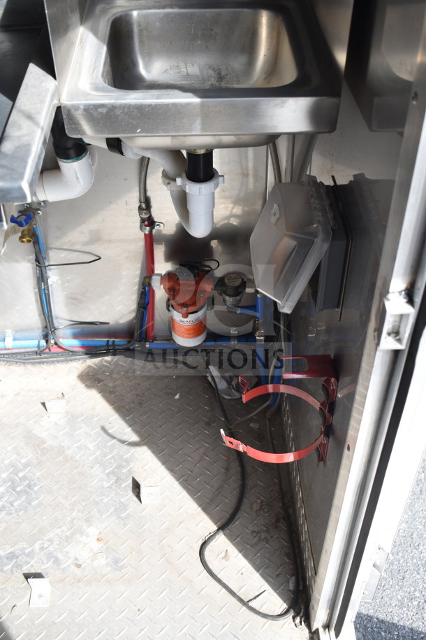 Under-sink area of 2021 Texino cooking trailer showing piping, filter, and wiring on metal floor.