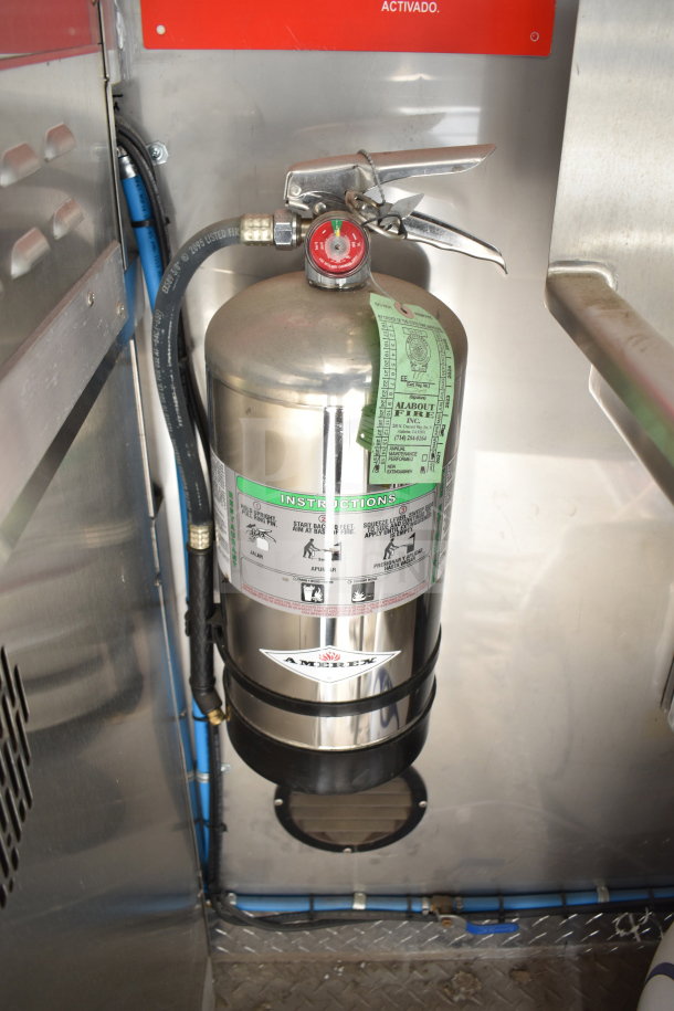 Shiny stainless steel Amerex fire extinguisher inside Texino cooking trailer, mounted on metal panel with attached instruction label.
