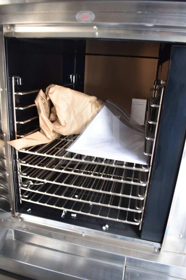 Interior view of a stainless steel cooking trailer oven with racks inside. Visible brochure and packaging materials.