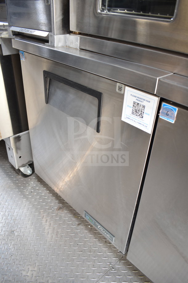 Texino cooking trailer interior showing stainless steel True refrigeration unit, equipped with caution labels and QR code tag.