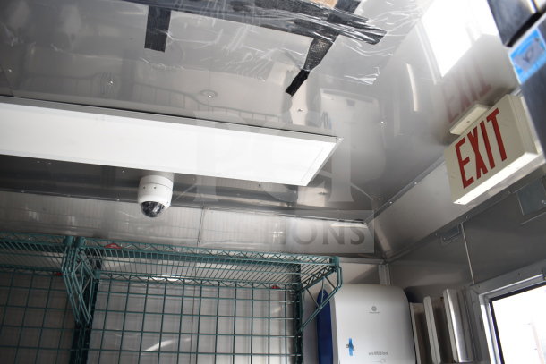 Interior of 2021 Texino 28ft Cooking Trailer with security camera, overhead lighting, wire shelf, and exit sign.