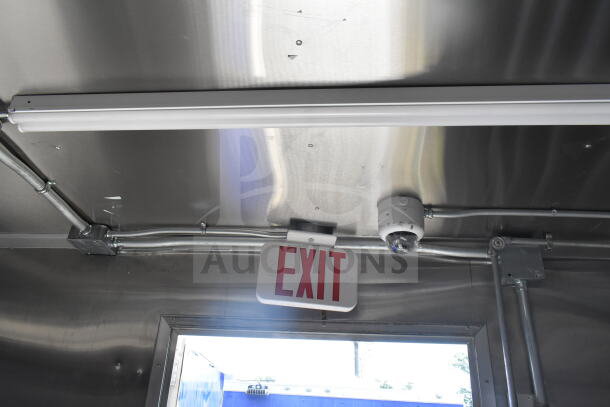 Interior view of Rock Solid Cargo food trailer shell, featuring CaptiveAire grease hood, exit sign, wiring, and mounted security camera.