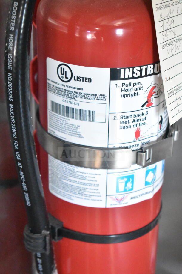 Red fire extinguisher with UL listing label, metal bracket, and instruction tag attached, part of auction item food trailer.