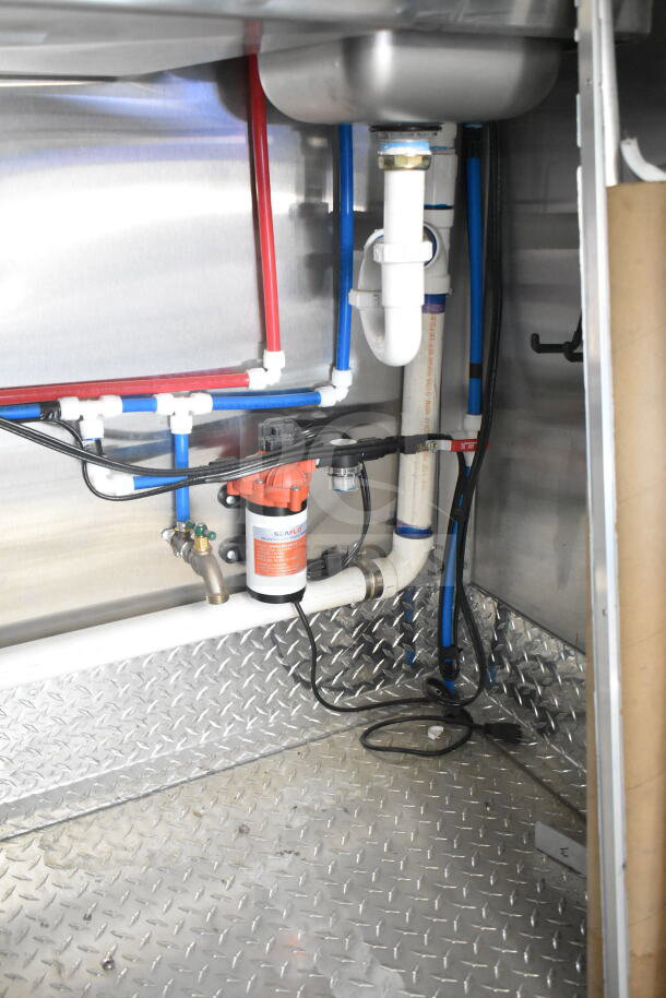 Interior of Rock Solid Cargo 8.5'x28' food trailer shell showing plumbing and Seaflo water pump installed on diamond plate flooring.