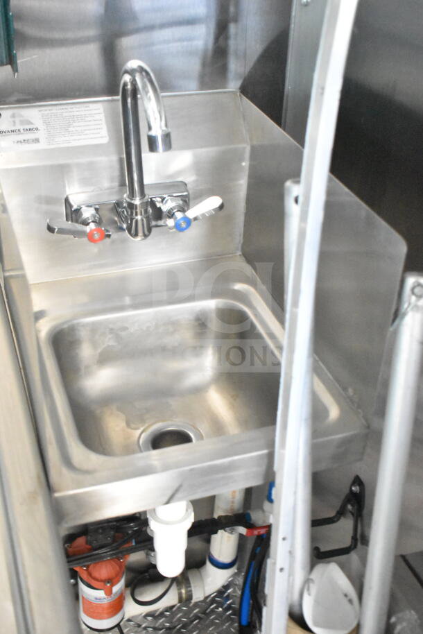 Rock Solid Cargo food trailer interior view, showcasing a stainless steel sink with faucet controls, piping, and labels.