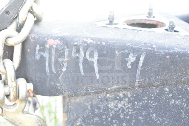 Close-up of a black metal surface with visible chains, bolts, and faint markings, possibly related to VIN identification.