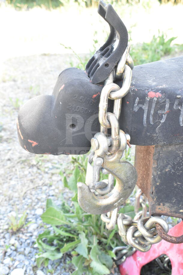 Close-up of trailer hitch with a heavy-duty chain and latch, part of Rock Solid Cargo food trailer shell. Visible wear on hitch.