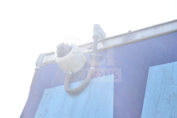 A close-up of a mounted security camera on a food trailer's exterior, under bright sunlight.