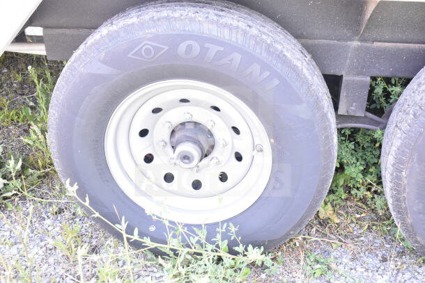 Close-up of Otani tire on Rock Solid Cargo trailer, resting on gravel with surrounding grass. Suitable for food trailer build.