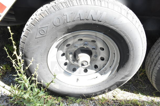 Rock Solid Cargo trailer wheel with Otani tire, showing lug nuts and metal rim. Ready for mobile restaurant use.